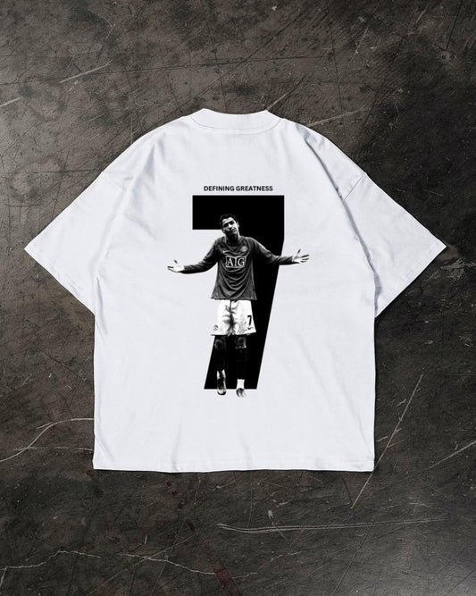 White t-shirt with a graphic of a Cristiano Ronaldo and 'Defying Greatness' text on a dark textured surface